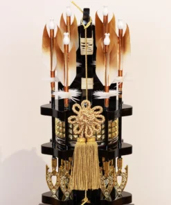 Japanese Hamaya arrow display with gold cord and tassel in black lacquer case, set against gold background with feathered arrows and symbolic ornaments. Wholesale by Fujiki Crafts.