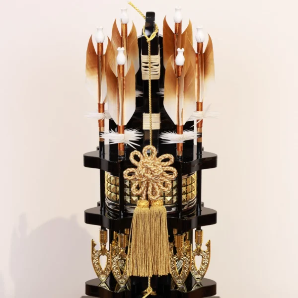 Japanese Hamaya arrow display with gold cord and tassel in black lacquer case, set against gold background with feathered arrows and symbolic ornaments. Wholesale by Fujiki Crafts.
