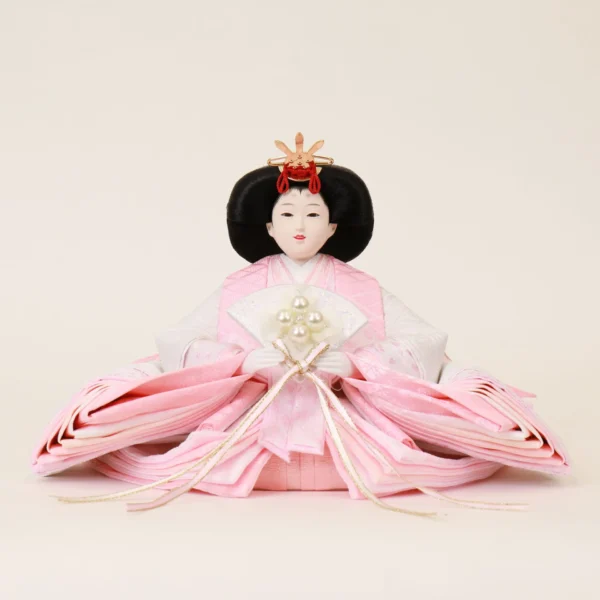 Japanese Hina Empress doll in soft pink and white kimono, holding pearl-decorated fan. Wholesale by Fujiki Crafts.