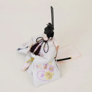 Emperor Hina doll in white patterned kimono with gold and purple accents, holding a ceremonial baton. Wholesale by Fujiki Crafts.