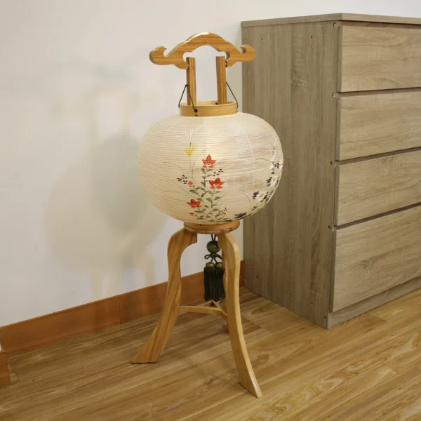 Handcrafted Japanese Bonbori lantern with washi paper shade, featuring hand-painted red spider lilies, wild daisies, and yellow rapeseed flowers on a natural wood stand. Wholesale by Fujiki Crafts.
