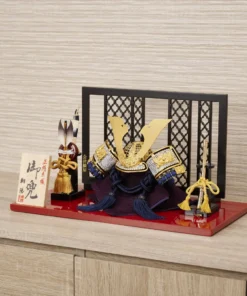 Japanese Kabuto helmet display with gold crest and silk thread navy strap on red lacquered base, featuring folding screen, miniature sword, and decorative arrows. Wholesale by Fujiki Crafts.