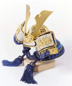 Japanese Kabuto helmet display with gold crest and silk thread navy strap on red lacquered base, featuring folding screen, miniature sword, and decorative arrows. Wholesale by Fujiki Crafts.