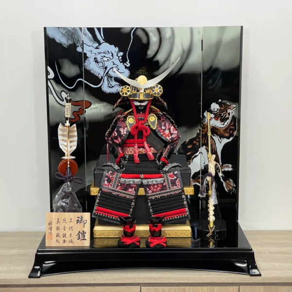 Handcrafted Japanese Samurai armor set in red and black, displayed with dragon and tiger backdrop. Wholesale by Fujiki Crafts
