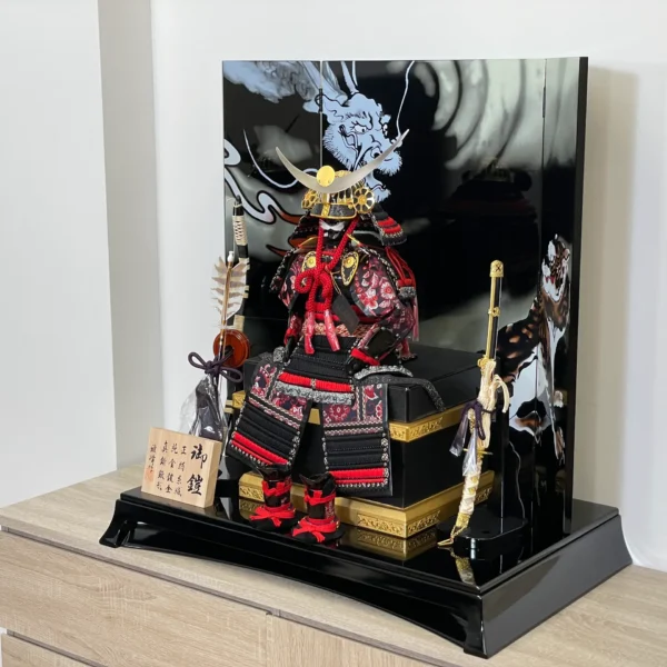 Handcrafted Japanese Samurai armor set in red and black, displayed with dragon and tiger backdrop. Wholesale by Fujiki Crafts