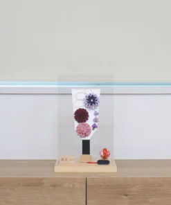Handcrafted Japanese Hagoita paddle in display case with soft pink and purple flowers, set on wooden base with Yuubi nameplate. Wholesale by Fujiki Crafts.