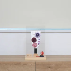 Handcrafted Japanese Hagoita paddle in display case with soft pink and purple flowers, set on wooden base with Yuubi nameplate. Wholesale by Fujiki Crafts.