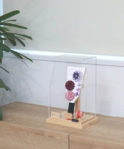 Handcrafted Japanese Hagoita paddle in display case with soft pink and purple flowers, set on wooden base with Yuubi nameplate. Wholesale by Fujiki Crafts.