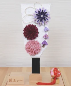 Handcrafted Japanese Hagoita paddle in display case with soft pink and purple flowers, set on wooden base with Yuubi nameplate. Wholesale by Fujiki Crafts.