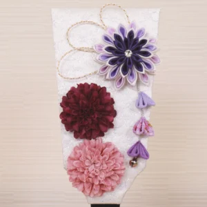 Handcrafted Japanese Hagoita paddle in display case with soft pink and purple flowers, set on wooden base with Yuubi nameplate. Wholesale by Fujiki Crafts.