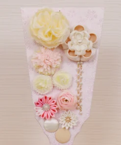 Handcrafted Japanese Hagoita paddle in pastel tones, decorated with white and pink tsumami flowers, presented in a clear acrylic display case with red handle and wooden base. Wholesale by Fujiki Crafts.