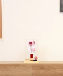 Handcrafted Japanese Hagoita paddle in soft pastel pink tones, adorned with white and pink tsumami kanzashi flowers, pearl accents, and decorative beads. Displayed in a clear acrylic case with wooden base. By Yuubi. Wholesale by Fujiki Crafts.