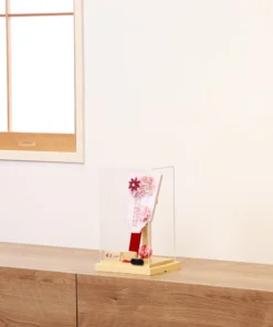 Handcrafted Japanese Hagoita paddle in soft pastel pink tones, adorned with white and pink tsumami kanzashi flowers, pearl accents, and decorative beads. Displayed in a clear acrylic case with wooden base. By Yuubi. Wholesale by Fujiki Crafts.