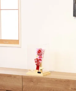 Traditional Japanese Hagoita paddle featuring vibrant red and white tsumami kanzashi flowers, sakura-patterned background, and hanging ornaments. Displayed in a clear acrylic case with wooden base, and decorative white rose accent. By Huka. Wholesale by Fujiki Crafts.