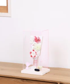 Handcrafted Japanese Hagoita paddle in white and soft pink tones, adorned with large fabric flowers and decorative beads. Set in a pink-edged clear acrylic case with a white base. Wholesale by Fujiki Crafts.