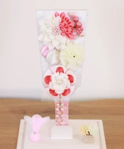 Handcrafted Japanese Hagoita paddle in white and soft pink tones, adorned with large fabric flowers and decorative beads. Set in a pink-edged clear acrylic case with a white base. Wholesale by Fujiki Crafts.