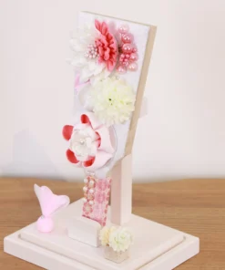 Handcrafted Japanese Hagoita paddle in white and soft pink tones, adorned with large fabric flowers and decorative beads. Set in a pink-edged clear acrylic case with a white base. Wholesale by Fujiki Crafts.