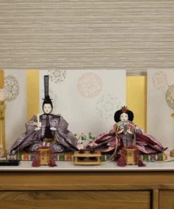 Elegant Japanese Hina doll set with plum and burgundy kimono, displayed on a white platform with gold-accented folding screen and lanterns. Wholesale by Fujiki Crafts.