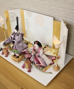 Elegant Japanese Hina doll set with plum and burgundy kimono, displayed on a white platform with gold-accented folding screen and lanterns. Wholesale by Fujiki Crafts.