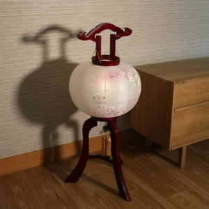 Handcrafted Japanese Chōchin lantern with cherry blossom design on white and lavender washi paper, displayed on wooden base. Wholesale by Fujiki Crafts.
