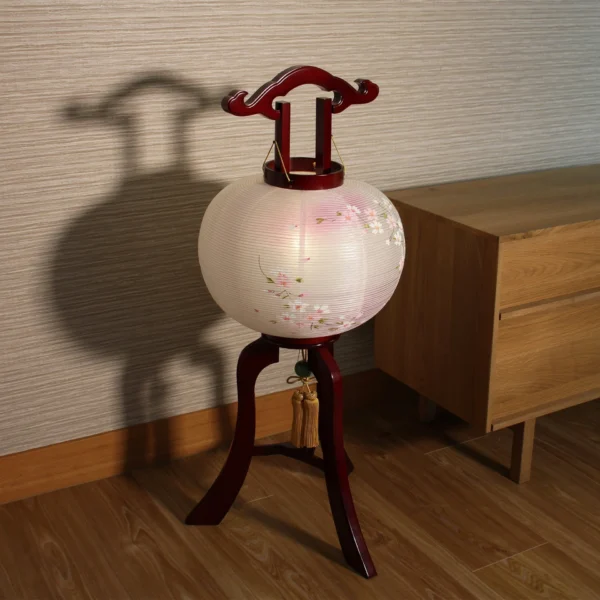 Handcrafted Japanese Chōchin lantern with cherry blossom design on white and lavender washi paper, displayed on wooden base. Wholesale by Fujiki Crafts.