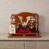 Handcrafted Japanese kabuto samurai helmet display with red cord and gold accents, set on a wooden stand with katana and arrows. Wholesale by Fujiki Crafts.