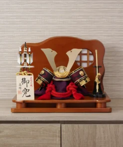 Handcrafted Japanese kabuto samurai helmet display with red cord and gold accents, set on a wooden stand with katana and arrows. Wholesale by Fujiki Crafts.