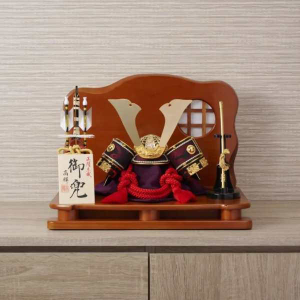 Handcrafted Japanese kabuto samurai helmet display with red cord and gold accents, set on a wooden stand with katana and arrows. Wholesale by Fujiki Crafts.