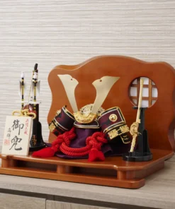 Handcrafted Japanese kabuto samurai helmet display with red cord and gold accents, set on a wooden stand with katana and arrows. Wholesale by Fujiki Crafts.