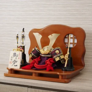 Handcrafted Japanese kabuto samurai helmet display with red cord and gold accents, set on a wooden stand with katana and arrows. Wholesale by Fujiki Crafts.