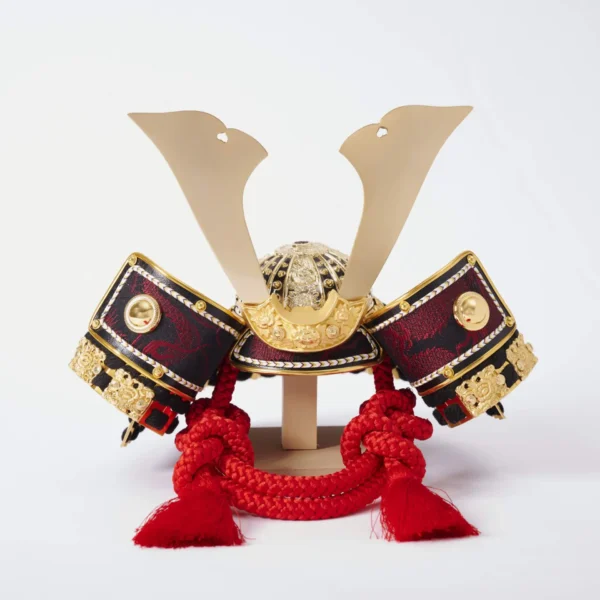 Handcrafted Japanese kabuto samurai helmet display with red cord and gold accents, set on a wooden stand with katana and arrows. Wholesale by Fujiki Crafts.