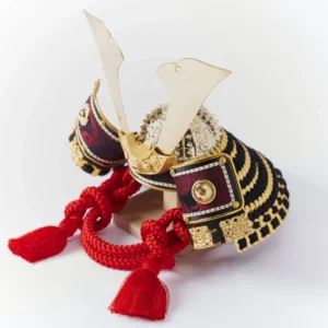 Handcrafted Japanese kabuto samurai helmet display with red cord and gold accents, set on a wooden stand with katana and arrows. Wholesale by Fujiki Crafts.