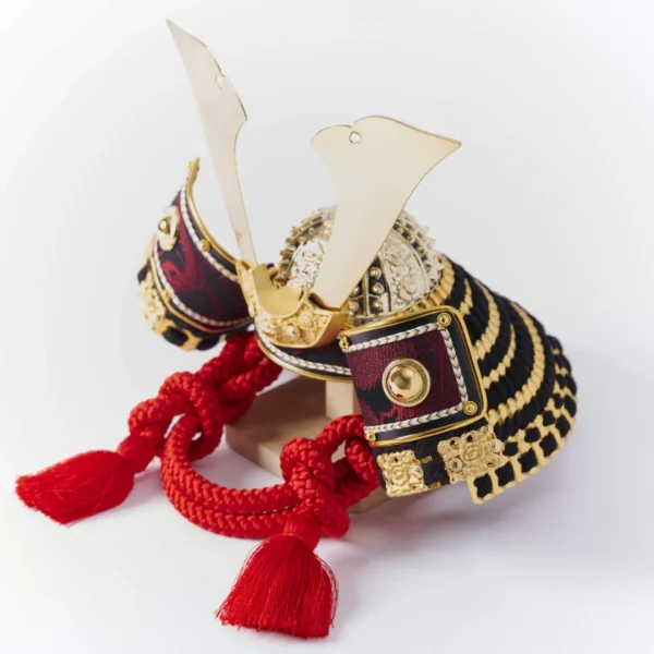 Handcrafted Japanese kabuto samurai helmet display with red cord and gold accents, set on a wooden stand with katana and arrows. Wholesale by Fujiki Crafts.