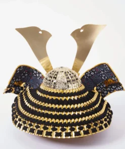 Handcrafted Japanese kabuto samurai helmet display with red cord and gold accents, set on a wooden stand with katana and arrows. Wholesale by Fujiki Crafts.