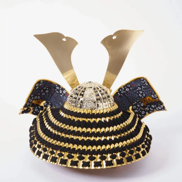Handcrafted Japanese kabuto samurai helmet display with red cord and gold accents, set on a wooden stand with katana and arrows. Wholesale by Fujiki Crafts.