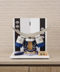 Japanese samurai kabuto helmet in silver with blue cords and tassels, mounted on a white and wood display stand with decorative folding screen. Wholesale by Fujiki Crafts.