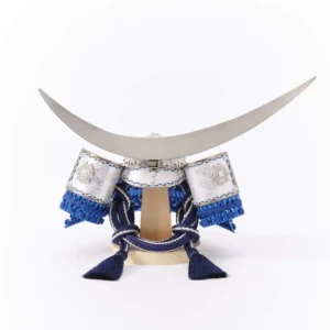 Japanese samurai kabuto helmet in silver with blue cords and tassels, mounted on a white and wood display stand with decorative folding screen. Wholesale by Fujiki Crafts.