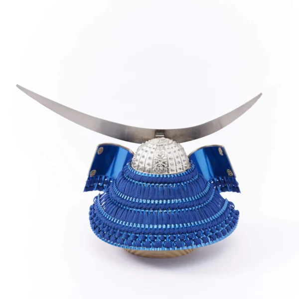 Japanese samurai kabuto helmet in silver with blue cords and tassels, mounted on a white and wood display stand with decorative folding screen. Wholesale by Fujiki Crafts.