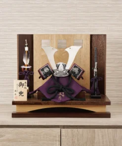 Traditional Kabuto samurai helmet with silver crest, mounted on a dark wood base, flanked by miniature sword and arrow display. Wholesale by Fujiki Crafts.