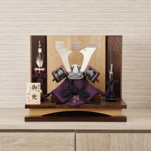 Traditional Kabuto samurai helmet with silver crest, mounted on a dark wood base, flanked by miniature sword and arrow display. Wholesale by Fujiki Crafts.