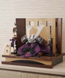 Traditional Kabuto samurai helmet with silver crest, mounted on a dark wood base, flanked by miniature sword and arrow display. Wholesale by Fujiki Crafts.
