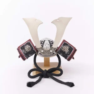 Traditional Kabuto samurai helmet with silver crest, mounted on a dark wood base, flanked by miniature sword and arrow display. Wholesale by Fujiki Crafts.