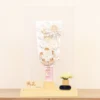 Elegant handcrafted Hagoita paddle adorned with white and beige Kanzashi flowers, set in a wooden base with acrylic case and soft floral accent. Wholesale by Fujikicrafts.