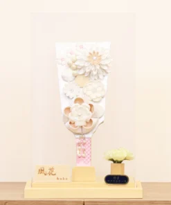Elegant handcrafted Hagoita paddle adorned with white and beige Kanzashi flowers, set in a wooden base with acrylic case and soft floral accent. Wholesale by Fujikicrafts.