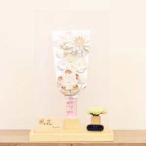 Elegant handcrafted Hagoita paddle adorned with white and beige Kanzashi flowers, set in a wooden base with acrylic case and soft floral accent. Wholesale by Fujikicrafts.