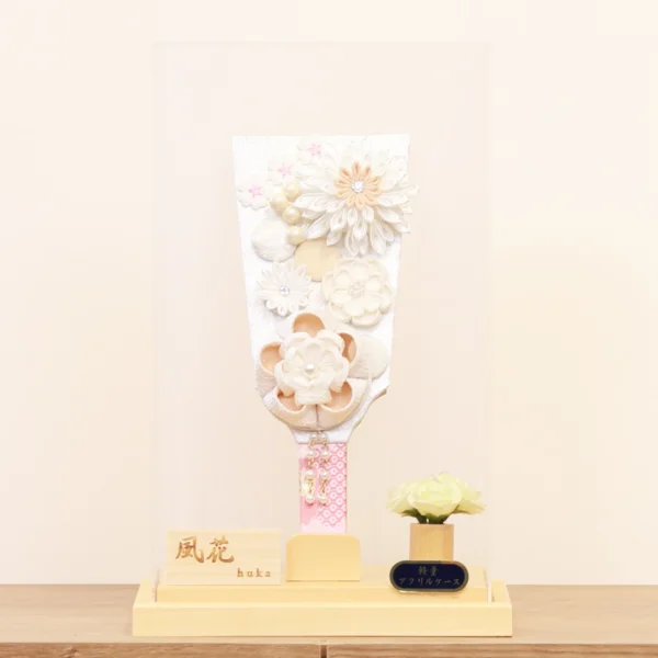 Elegant handcrafted Hagoita paddle adorned with white and beige Kanzashi flowers, set in a wooden base with acrylic case and soft floral accent. Wholesale by Fujikicrafts.