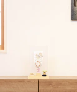 Elegant handcrafted Hagoita paddle adorned with white and beige Kanzashi flowers, set in a wooden base with acrylic case and soft floral accent. Wholesale by Fujikicrafts.