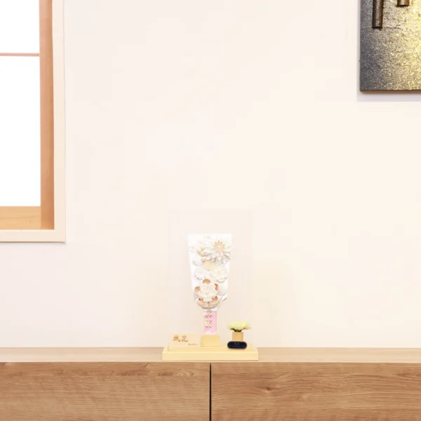 Elegant handcrafted Hagoita paddle adorned with white and beige Kanzashi flowers, set in a wooden base with acrylic case and soft floral accent. Wholesale by Fujikicrafts.