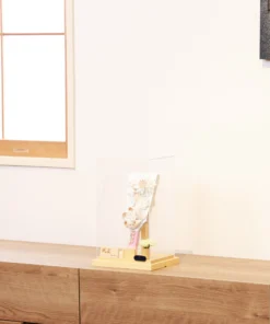 Elegant handcrafted Hagoita paddle adorned with white and beige Kanzashi flowers, set in a wooden base with acrylic case and soft floral accent. Wholesale by Fujikicrafts.