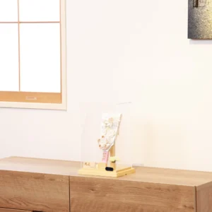 Elegant handcrafted Hagoita paddle adorned with white and beige Kanzashi flowers, set in a wooden base with acrylic case and soft floral accent. Wholesale by Fujikicrafts.
